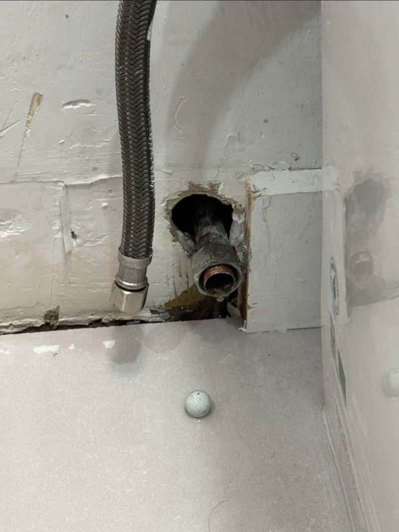 Photo Julian Esses attached to his 10 June email: a braided supply line hanging free, the water pipe where it leaves the wall with the wall opened around it, and a small round white object on the floor below.